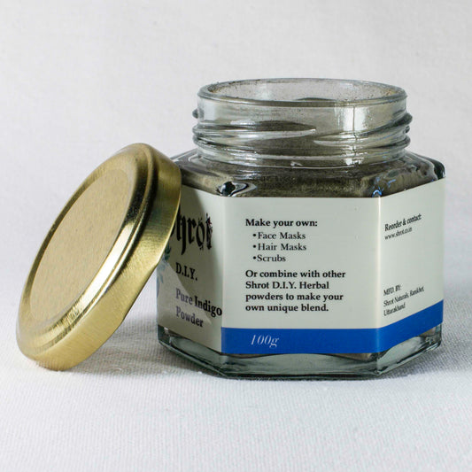 Glass jar with gold lid labeled 'Shrot Pure Indigo Powder' on a white background. Side angle, with lid off.