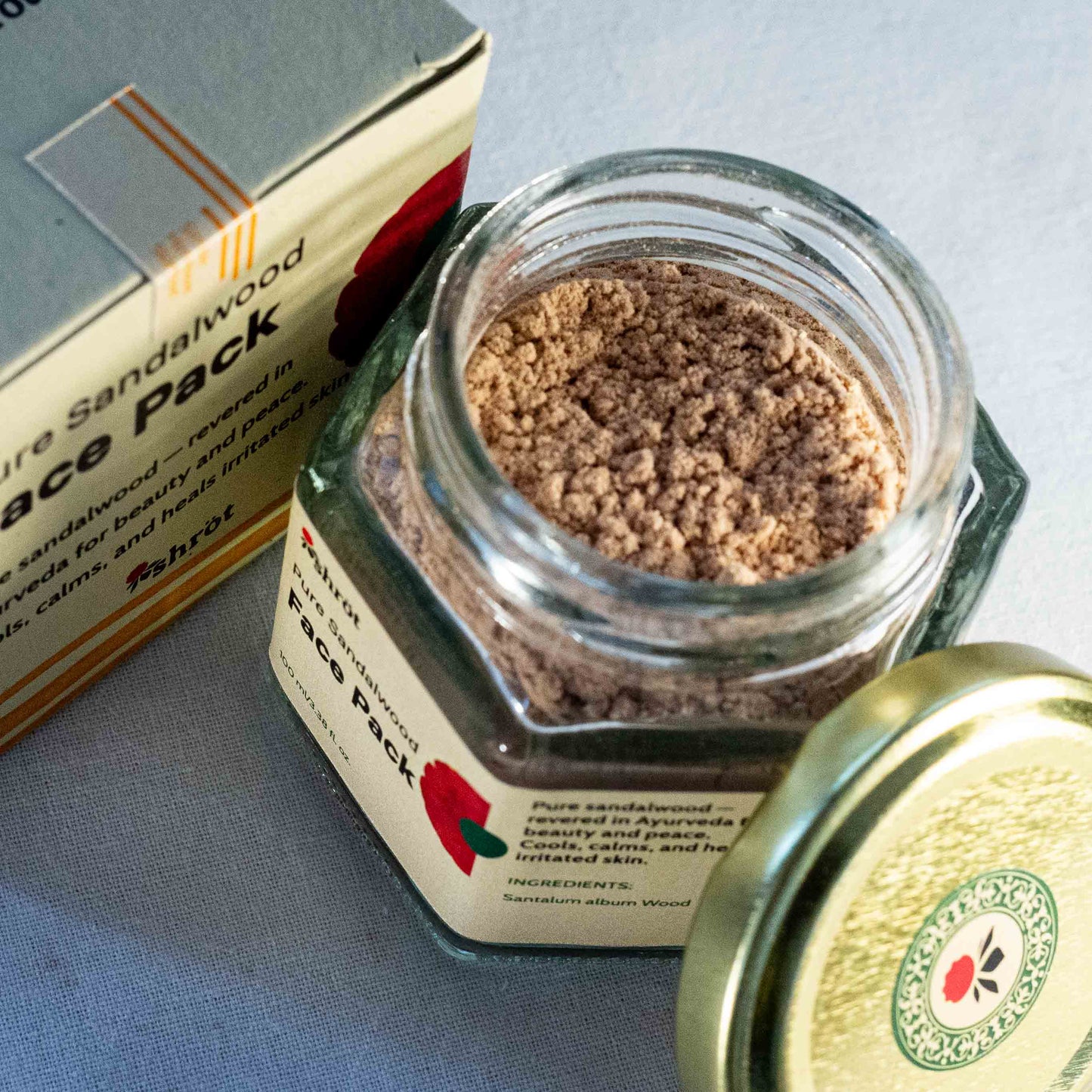 Glass jar with sandalwood face pack Shrot Natural beauty products and packaging on a blue surface