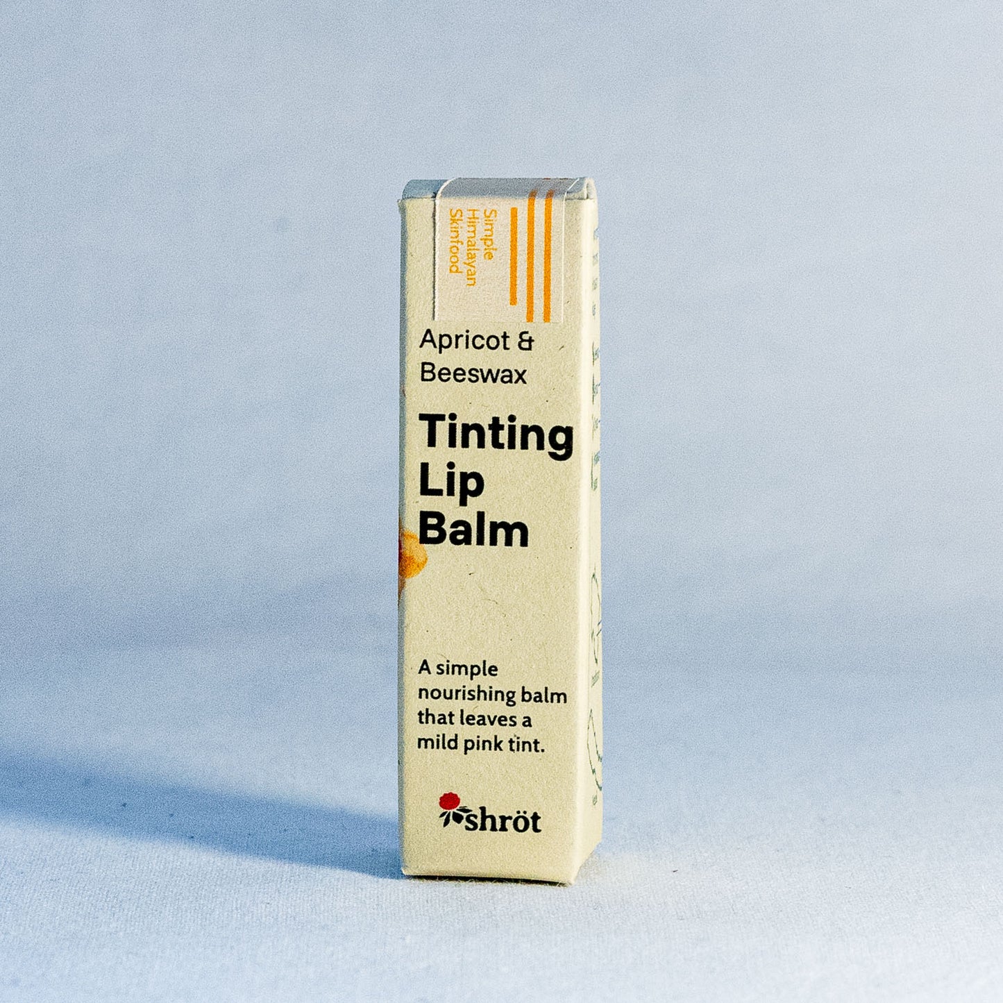 Tinting lip balm packaging with apricot and beeswax ingredients by a natural skincare brand called Shrot on a light blue background